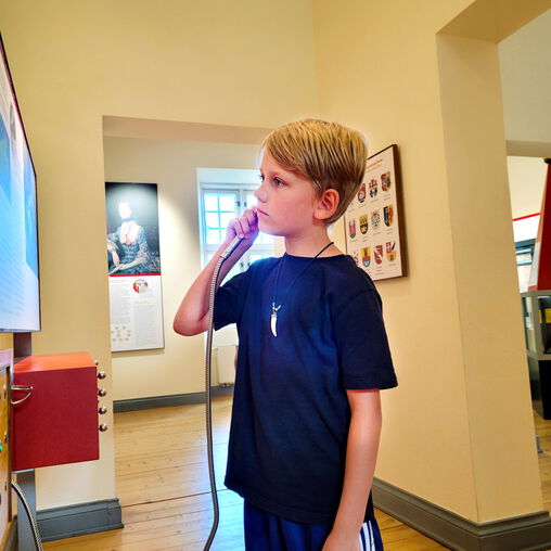 Junge steht vor einer interaktiven Wand und hält Hörer ans Ohr