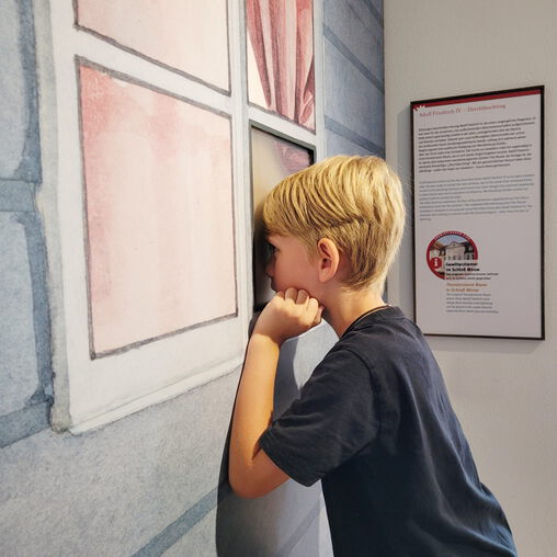 Junge schaut durch ein Fenster einer Ausstellungswand