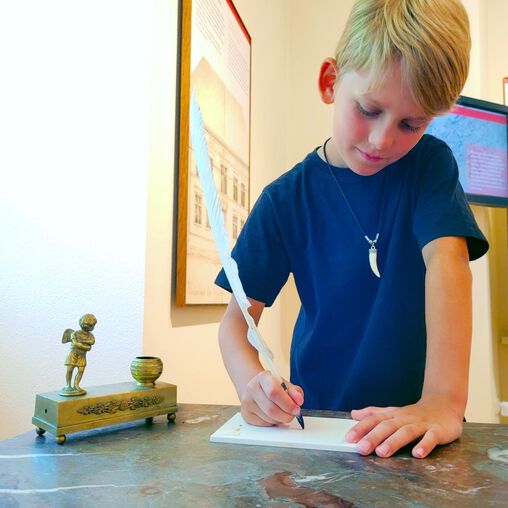 Junge schreibt mit einer Feder auf einem Blatt Papier
