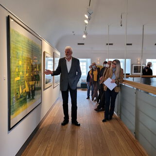 Der Künstler Gerd Frick erklärt einigen Besuchern ein Gemälde seiner Ausstellung.