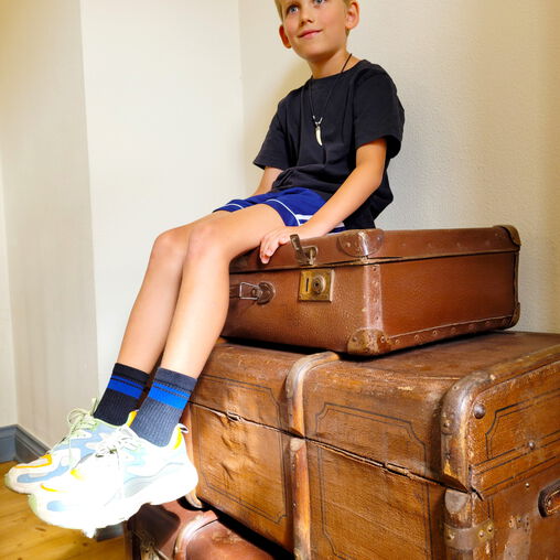 Junge sitzt auf 3 alten braunen Koffern der Ausstellung
