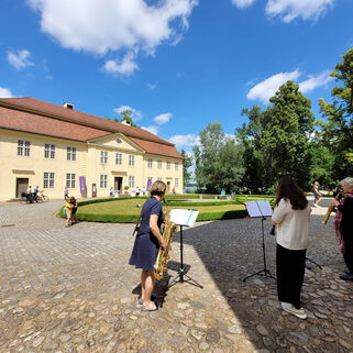 3 Musikerinnen mit Blasinstrumenten vor dem 3 Königinnen Palais bei schönem Wetter